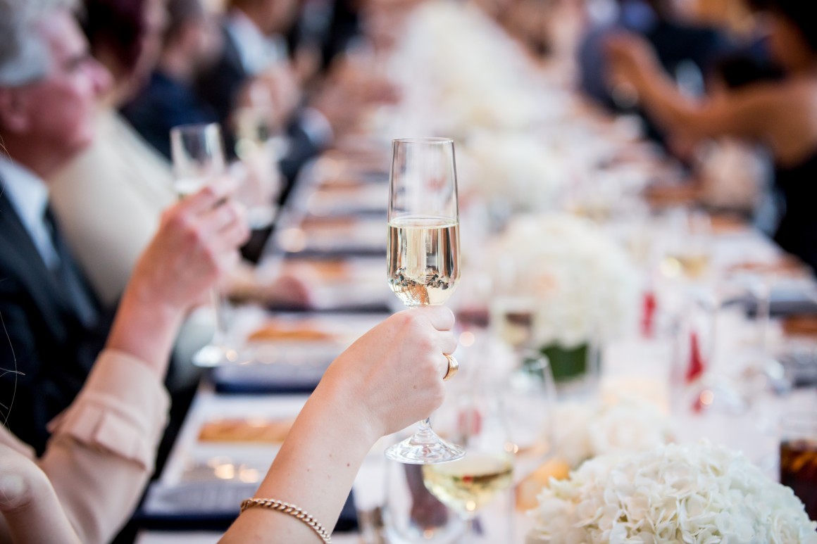 Wedding guests at table raise champagne glasses to toast newlyweds
