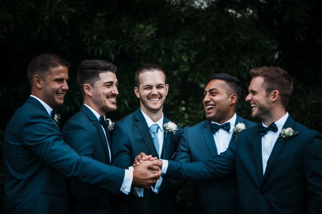 Groom and groomsmen join hands to celebrate wedding day